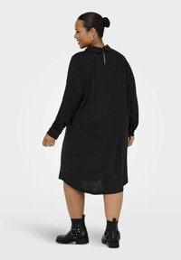 Černé šaty s dlouhými rukávy a volným střihem, s detaily klíčové dírky na zádech a knoflíkovými manžetami. V kombinaci s černými kotníkovými botami.