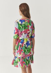 Bloemjurk met korte mouwen, met een levendig patroon van roze, blauwe en groene bloemen op een lichte achtergrond, en een gelaagde zoom.
