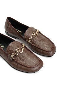 Brązowe mokasyny ze skóry o teksturowanej powierzchni, złotych zdobieniach i zaokrąglonym nosku. Podeszwy są płaskie i gładkie.