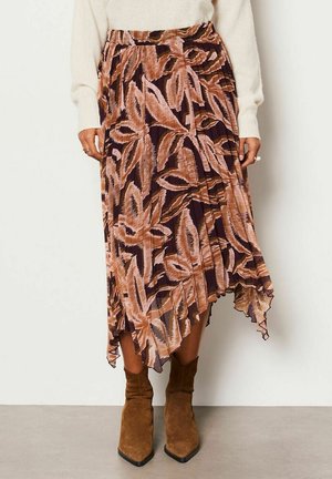 Jupe midi plissée avec motif abstrait de feuilles marron et beige, associée à des bottines en daim marron et des manches de pull crème visibles.