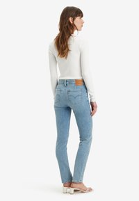 Jean en denim bleu clair avec une coupe slim, patch en cuir à l'arrière et deux poches arrière. Associé à un haut ajusté à manches longues blanc côtelé.