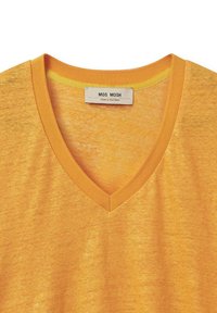 Camiseta amarilla de cuello en V con una textura suave y cuello acanalado; la etiqueta dice "MOS MOSH". Tejido ligeramente texturizado con variaciones sutiles.