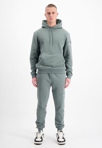 Lichtgroen sweatshirt met capuchon en voorzak, gecombineerd met bijpassende joggingbroek. Stof lijkt zacht; heeft elastische boorden en tailleband.