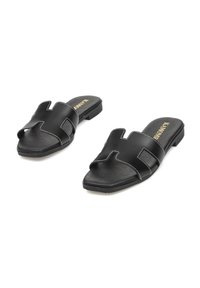 Sandalias negras con un diseño de punta cuadrada, elaboradas en cuero sintético. Cuentan con correas con recortes y un detalle de costura blanca contrastante.