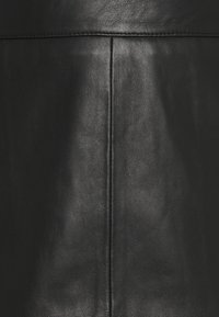 Fekete texturált bőr közeli kép központi függőleges varrással és a tetején egy vízszintes öltéssel.