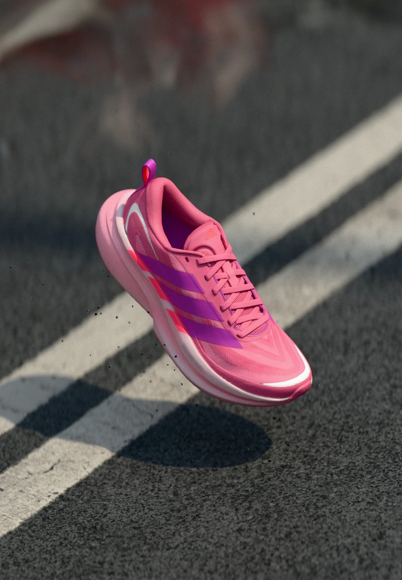 Pink and purple running shoe mid-air above asphalt road with white lane markings, small debris visible around shoe.