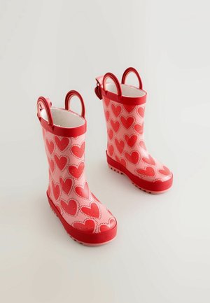 Bottes de pluie en caoutchouc rouge avec motifs de cœurs roses, texture lisse, bout arrondi, et deux anses pour un enfilage facilité.