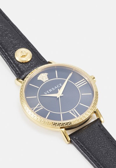 Gold-tone watch with a dark blue dial, Roman numeral markers, and textured black leather strap featuring a gold accent button.