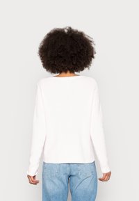 Pull en maille côtelée rose clair avec une coupe décontractée, un col rond et des manches longues, associé à un jean bleu clair ample.