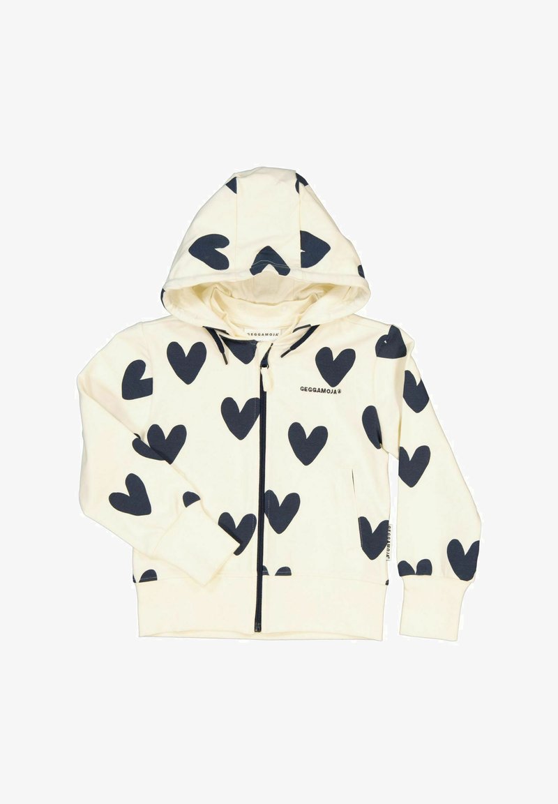 Zip hoodie, krämfärgad tyg med stora marinblå hjärtmönster, långa ärmar, framfickor och en huva med dragsko. Märkesetikett synlig på insidan.