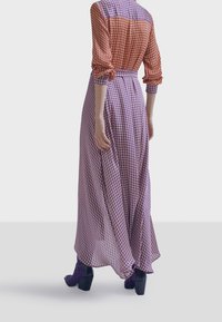 Vestido maxi con un patrón de cuadros rojo y púrpura, tela ligera, mangas largas, cintura ceñida y falda vaporosa. Botas de tacón grueso negras.