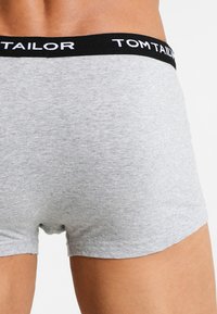 Grau Baumwoll-Boxershorts mit einem schwarzen Bund und weißem Markenlogo. Der Stoff wirkt weich mit einer glatten Textur.