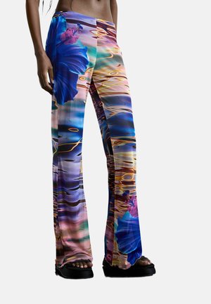 Hose mit bunten abstrakten und floralen Mustern, getragen von einer Person, kombiniert mit schwarzen Plateau-Sandalen.