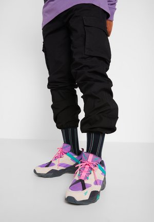 Person wearing black cargo pants with elastic cuffs, striped black socks, and multicolored sneakers in purple, pink, beige, and teal.