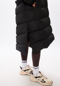 Black puffer coat with quilted design and snap buttons, paired with brown leggings and cream sneakers with black accents and striped socks.