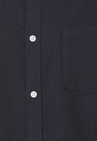 Camicia blu navy realizzata in tessuto con una sottile texture, dotata di bottoni bianchi e una tasca sul petto sul lato sinistro.
