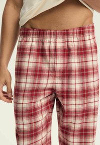 Czerwono-białe w kratę spodnie piżamowe z elastycznym pasem, wykonane z miękkiego, gładkiego materiału o luźnym kroju.