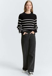 Svartvitrandig stickad tröja med ribbad struktur, kombinerad med högmidjade svarta byxor med vida ben och svarta sneakers.