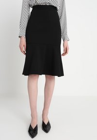 Svart utsvängd kjol i stretchmaterial med en åtsittande midja och en mjuk textur. Matchas med en randig blus med långa ärmar.