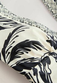 Gros plan d'un tissu à motif floral noir et blanc avec des fronces, mettant en valeur la texture et le design complexe de la bordure.