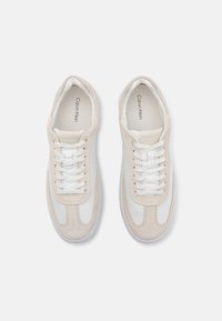 Sneakers bianchi e beige realizzati in materiali scamosciati e in pelle, con punte arrotondate, linguette imbottite e chiusura con lacci. Visibile il marchio Calvin Klein.