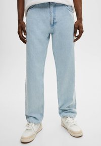 Jeans de mezclilla azul claro con corte recto. Presentan un bolsillo frontal y un cierre de botón, combinados con zapatillas blancas para un look casual.