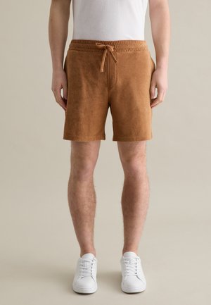 Brown terry cloth shorts with a drawstring waistband, featuring a relaxed fit. Paired with white sneakers, set against a neutral background.