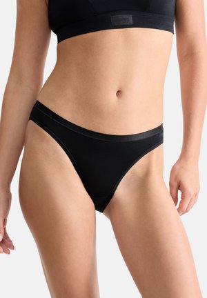 Donna che indossa biancheria intima nera senza cuciture stile bikini e reggiseno sportivo nero coordinato, mostrata dalla metà del busto fino alla parte superiore delle cosce.