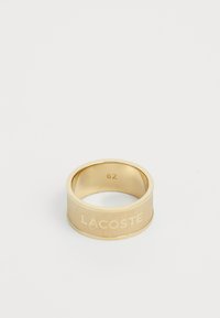 Zlatni prsten s zaobljenom trakom, posjeduje teksturiranu površinu i ugravirani logo "LACOSTE", veličina 62. Glačana unutarnja obrada.