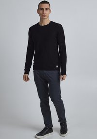 Zwarte langlopende shirt, slim fit, ronde hals. Gepaarde met marineblauwe broek en zwarte sneakers, met een soepele textuur en een minimalistisch ontwerp.