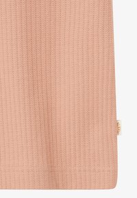 Detailný záber na broskyňovo zafarbenú ribbovanú pleteninu s malou bielou a oranžovou štítkom značky na okraji.