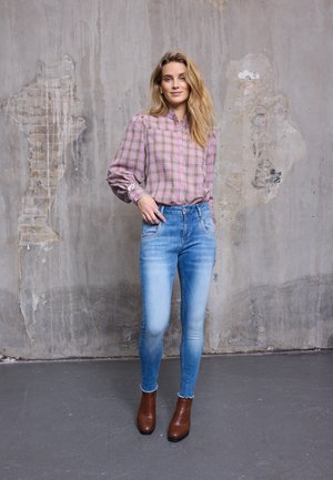 Pink és zöld tónusú kockás ing, világoskék skinny farmer, barna bokacsizma, texturált szürke fal háttérrel.