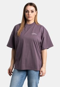 Camiseta oversized morada con mangas cortas, cuello redondo y texto bordado en blanco en el frente. Fabricada con suave algodón.