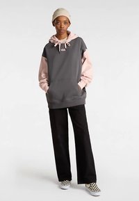 Grå og lyserød hættetrøje med stor forlompe, afslappet design, kombineret med sorte bukser og ternede slip-on sko.