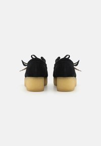 Pantofi din suede negri cu vârful rotunjit și toc scurt. Caracteristici includ șireturi în contrast și o talpă texturată. Design simplu, fără modele.
