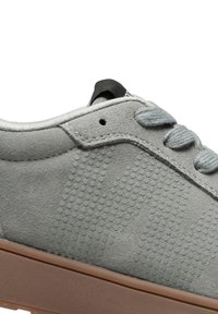 Grå mockasnörsko med rund tå, texturerad yta med prickmönster, grå snörning och brun gummisula. Svart dragflik på baksidan.