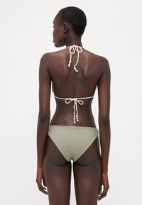 Komplet bikinija u svijetlo maslinastoj zelenoj boji, sa halter vezivanjem i dekorativnim perlicama. Jednostavna, glatka tekstura, minimalistički dizajn.