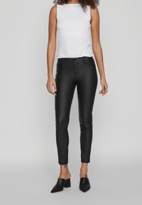 Pantalon en cuir noir coupe slim avec jambes fuselées, associé à un haut blanc sans manches ajusté et des mules noires à talons.