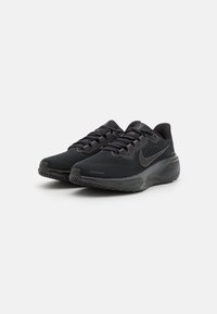 Baskets noires de sport avec une tige en mesh, une finition texturée, des lacets contrastés et une semelle en caoutchouc. Présente un logo Nike sur le côté.
