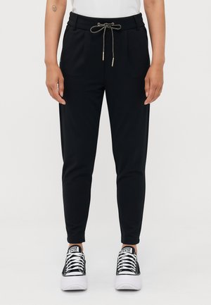 Svart joggebukser med snor i livet, med sidelommer og smalere ben. Materialet har en glatt tekstur. Brukt med svart og hvite sneakers.
