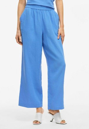 Lichtblauwe wijde broek met een elastische tailleband, gestructureerde stof en zijzakken, gecombineerd met grijze hakken.