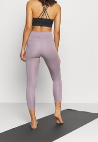 Sportivo nero con spalline incrociate, abbinato a leggings viola chiaro, texture liscia, design aderente e lunghezza cropped.