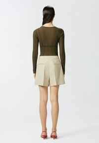 Maslinasto zelena majica dugih rukava s rebrastom teksturom uparena s laganim bež kratkim hlačama s džepovima i opuštenim krojem.