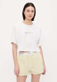 Wit cropped t-shirt met 'Calvin Klein' logo in regenboogkleuren. Gecombineerd met lichtgele shorts met een witte logo tailleband.