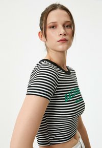 Top corto a rayas en blanco y negro de tela acanalada, con mangas cortas y un diseño gráfico en verde en la parte delantera.