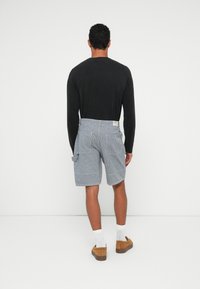 Striped blue shorts with front pockets, a tab on the side, and a label at the back, paired with a black long-sleeve shirt and brown shoes.
