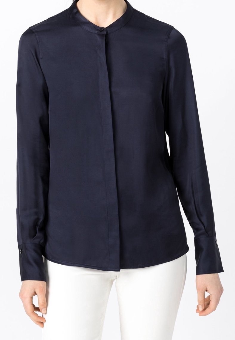 Blouse en soie bleu marine avec un col montant, une patte de boutonnage à l'avant et des manches longues. Elle présente des détails de boutons aux poignets et une texture lisse.