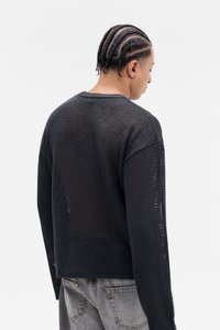 Svart strikket genser med en løs, åpen vevstruktur, med rund hals og lett senkede skuldre, kombinert med grå jeans.