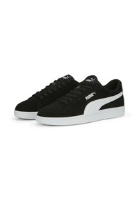 Une paire de baskets noires Puma avec une bande et une semelle blanches, dotées de lacets et du logo Puma sur le côté et sur la languette.