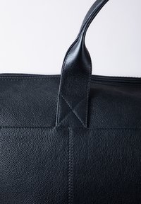 Black leather tote bag with a textured surface, featuring a sturdy handle and an exposed zipper along the top edge.